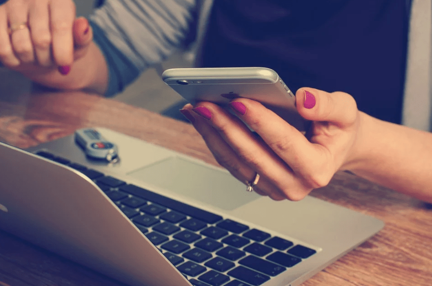 a hand holding an iPhone, and a laptop