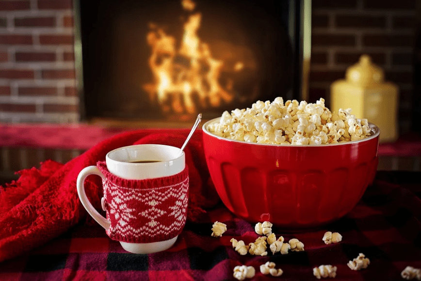 popcorn in a red bowl, a cup of coffee on the table, lit fireplace behind