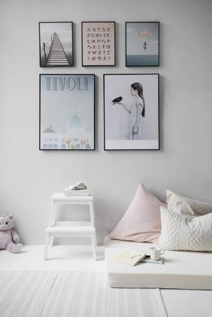 a wall with different posters, a mattress with pillows, and a small table