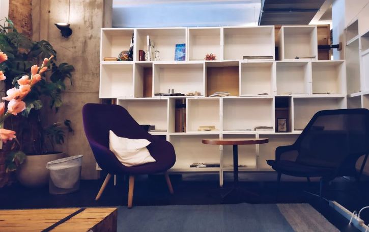 open cabinets on the wall; two chairs and a small table; plants at the left corner