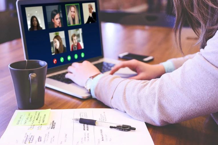 A woman attended a virtual office conference on zoom with a cup of coffee and notes on the table.