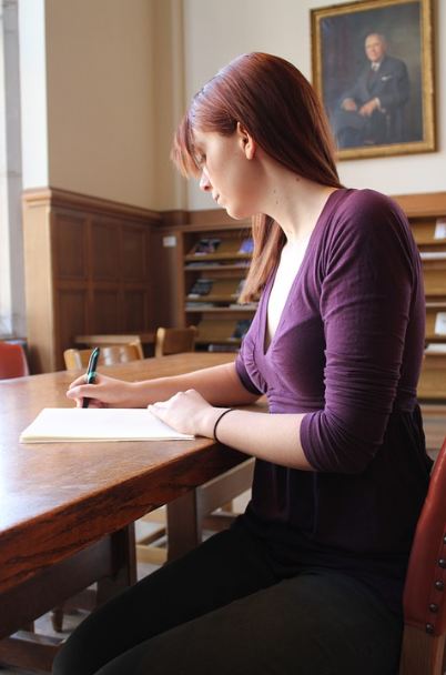 A woman sitting, and writing on her notebook