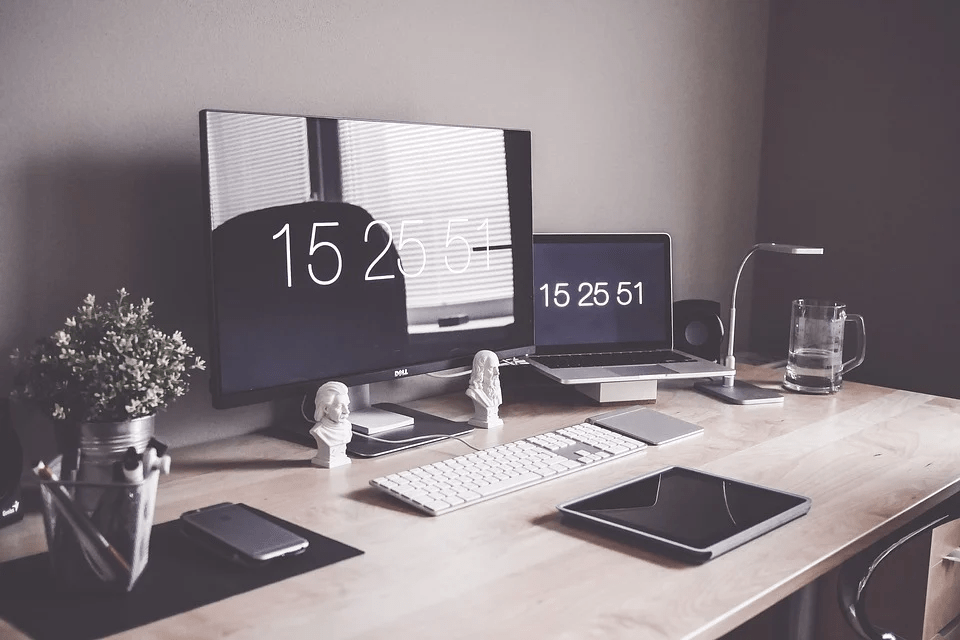 a desk with 2 computers, a tablet, a mug, a desk lamp, a plant