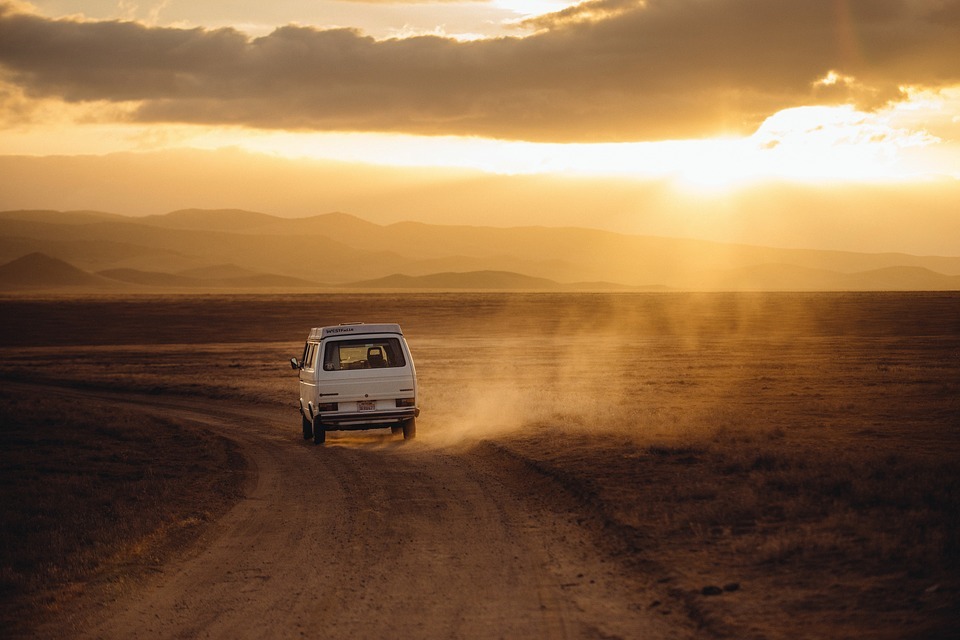 white van, dusty road, grass, mountains, clouds, sunlight peeking through the clouds