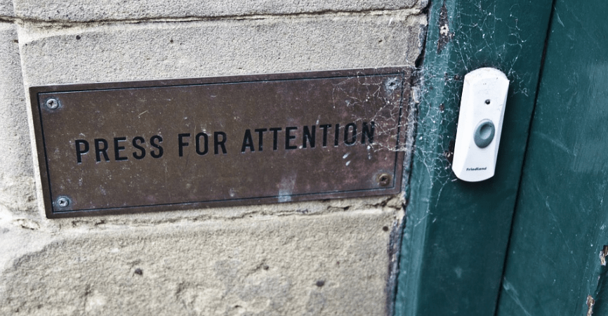 white doorbell buzzer, “press for attention” card on the wall, cement wall