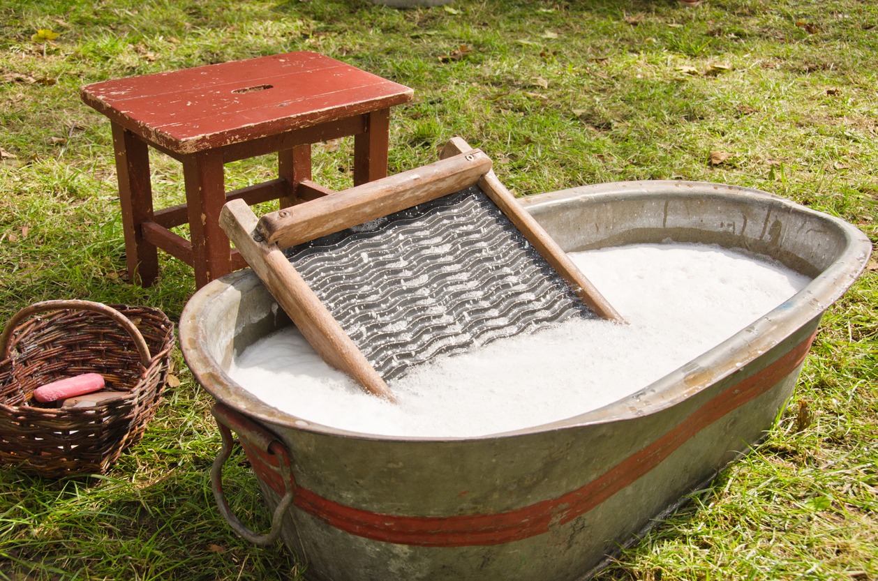a vintage washboard in a tub with soapy water, a wooden stool, a soap in a basket, green grass