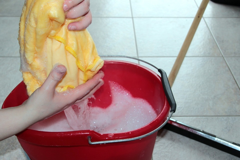 hands wringing a rug on a cleaning bucket with soapy water