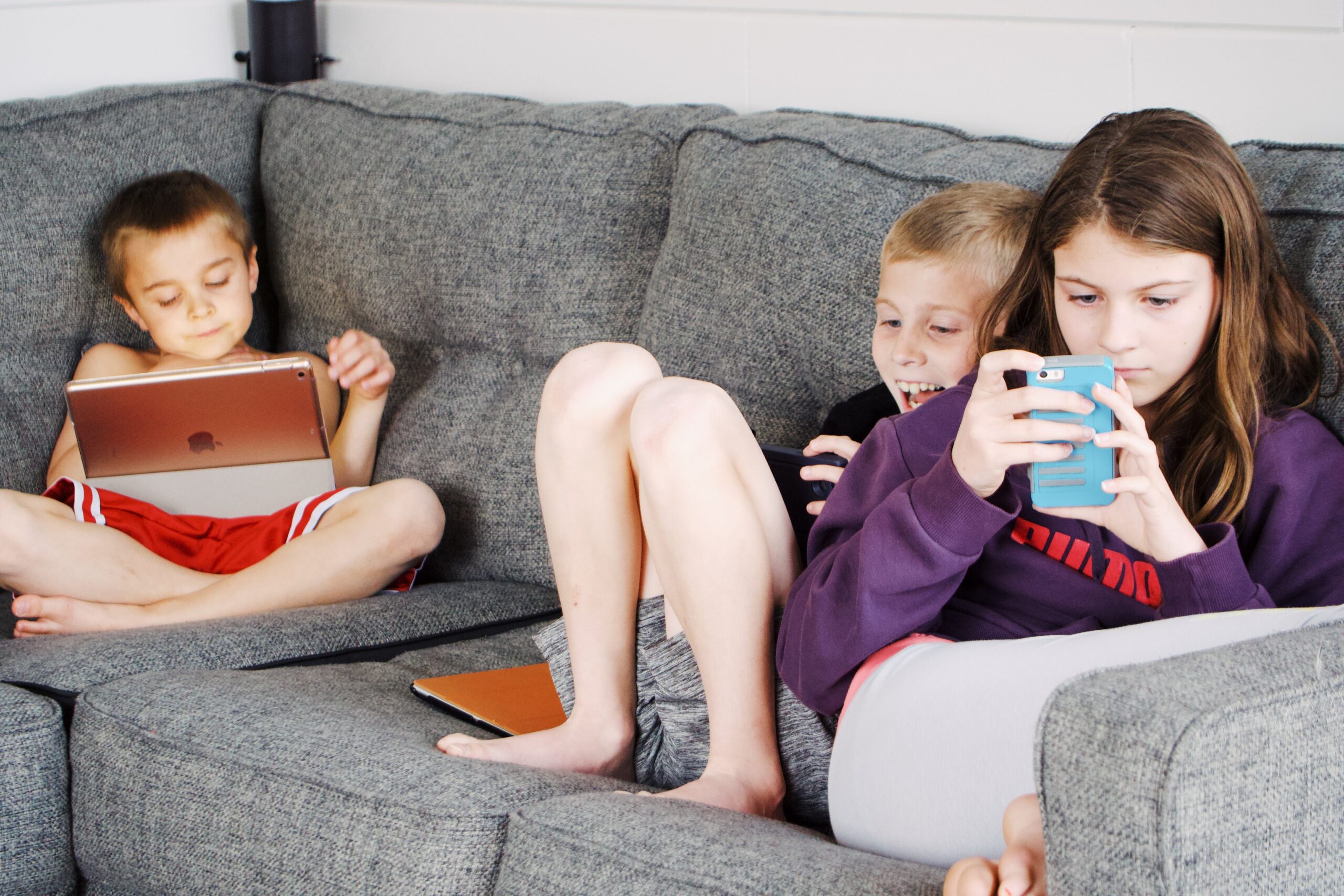 children lying on the sofa and using gadgets